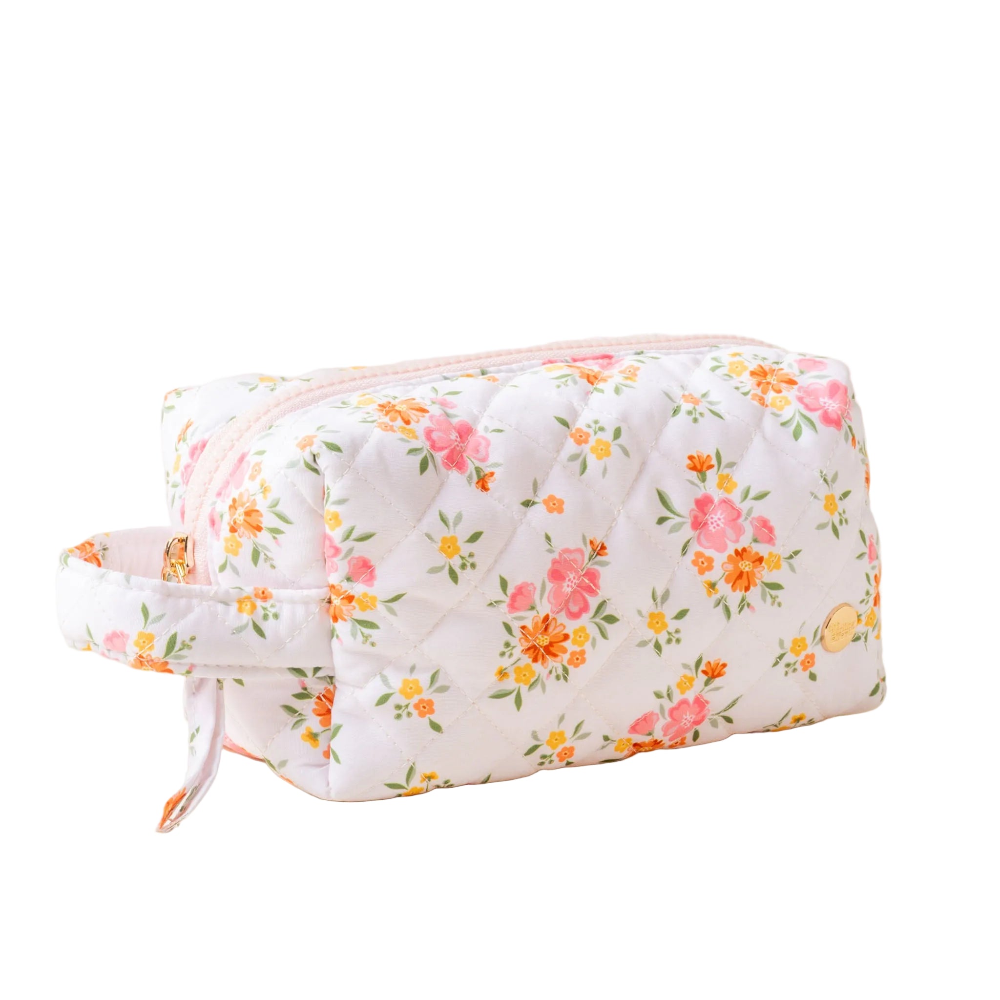 A quilted cosmetic pouch with a floral pattern, featuring a gold zipper and a carrying handle. Available at Be Charmed