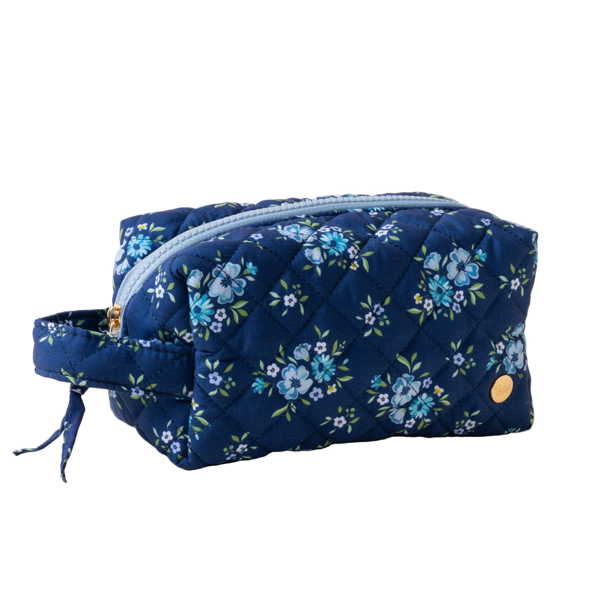 A quilted cosmetic pouch with a floral pattern, featuring a gold zipper and a carrying handle. Available at Be Charmed