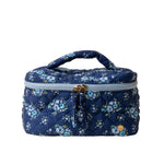 A quilted cosmetic bag with a floral pattern, a pink handle, and a double gold zipper. Available at Be Charmed