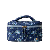 A quilted cosmetic bag with a floral pattern, a pink handle, and a double gold zipper. Available at Be Charmed