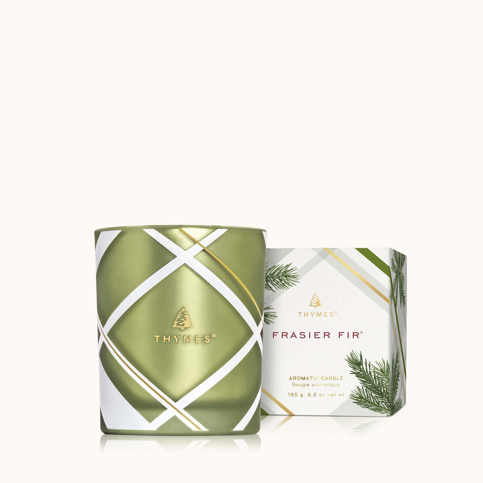 A Thymes Frasier Fir frosted plaid candle in green and white packaging, with the brand logo and product name visible. Available at Be Charmed