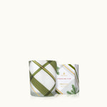 A square-shaped Thymes Frasier Fir frosted plaid votive candle in a white container with green and gold geometric patterns. Available at Be Charmed