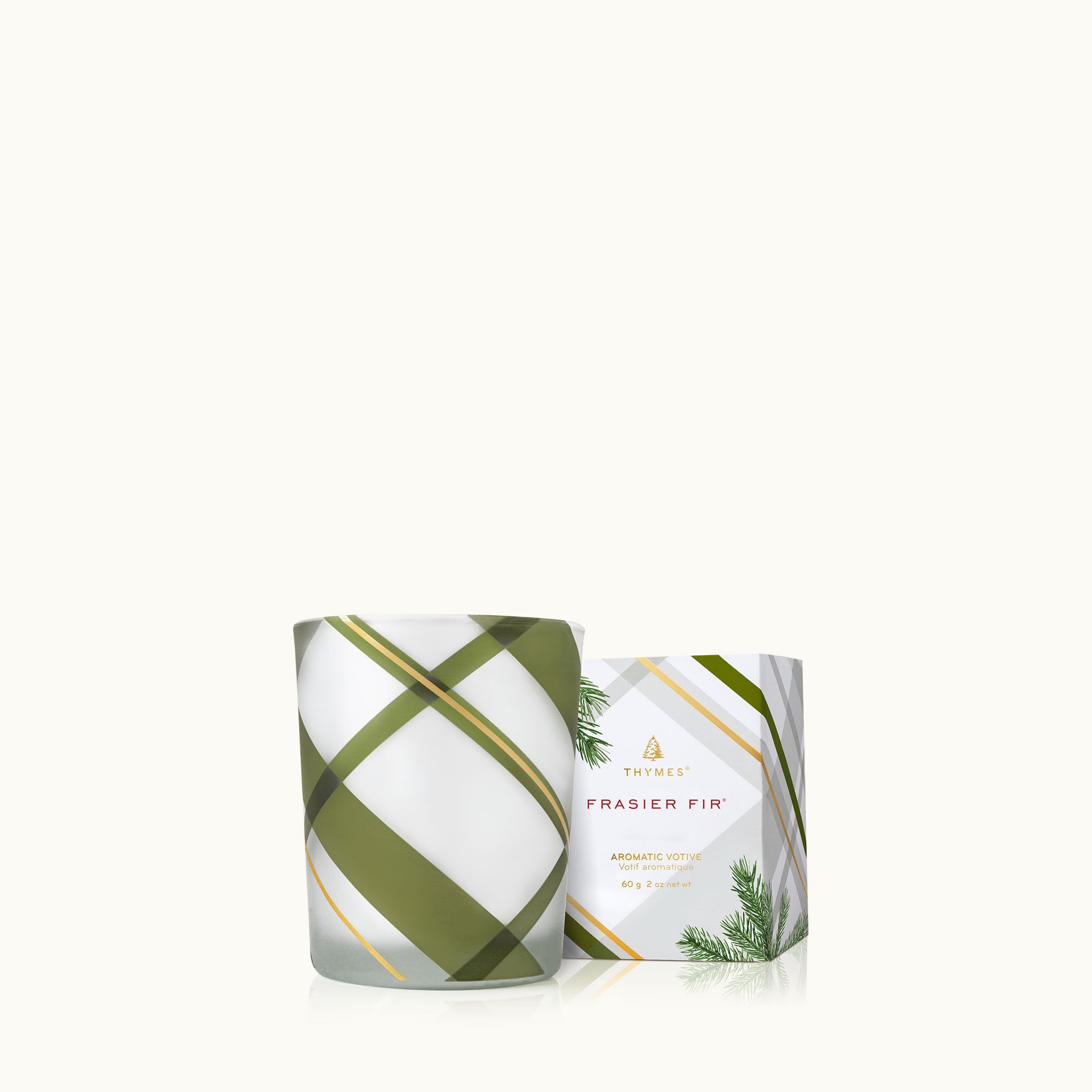 A square-shaped Thymes Frasier Fir frosted plaid votive candle in a white container with green and gold geometric patterns. Available at Be Charmed