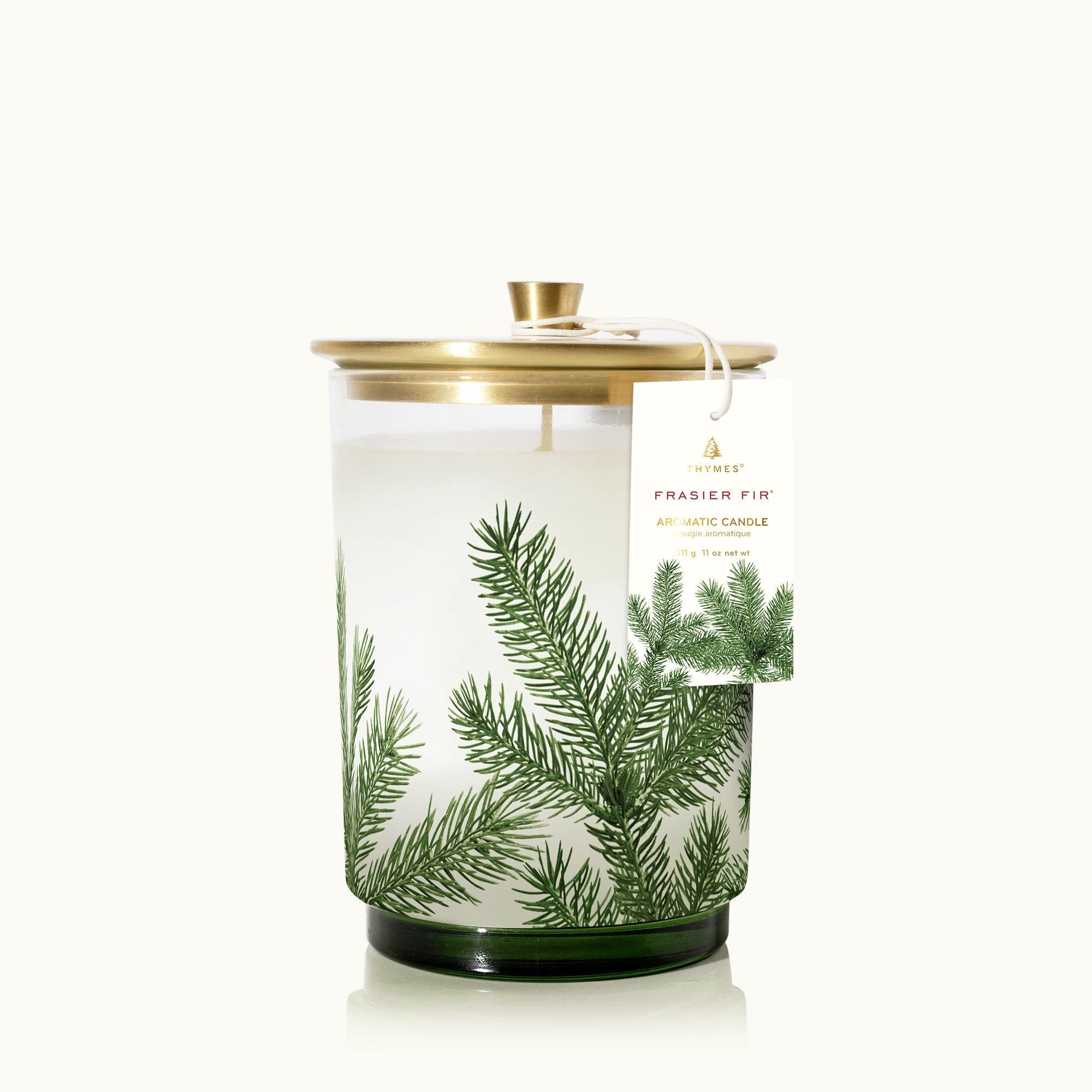 A clear glass candle with a lid and a label that reads 'Thymes Frasier Fir Pine Needle' with a green and white design. Available at Be Charmed