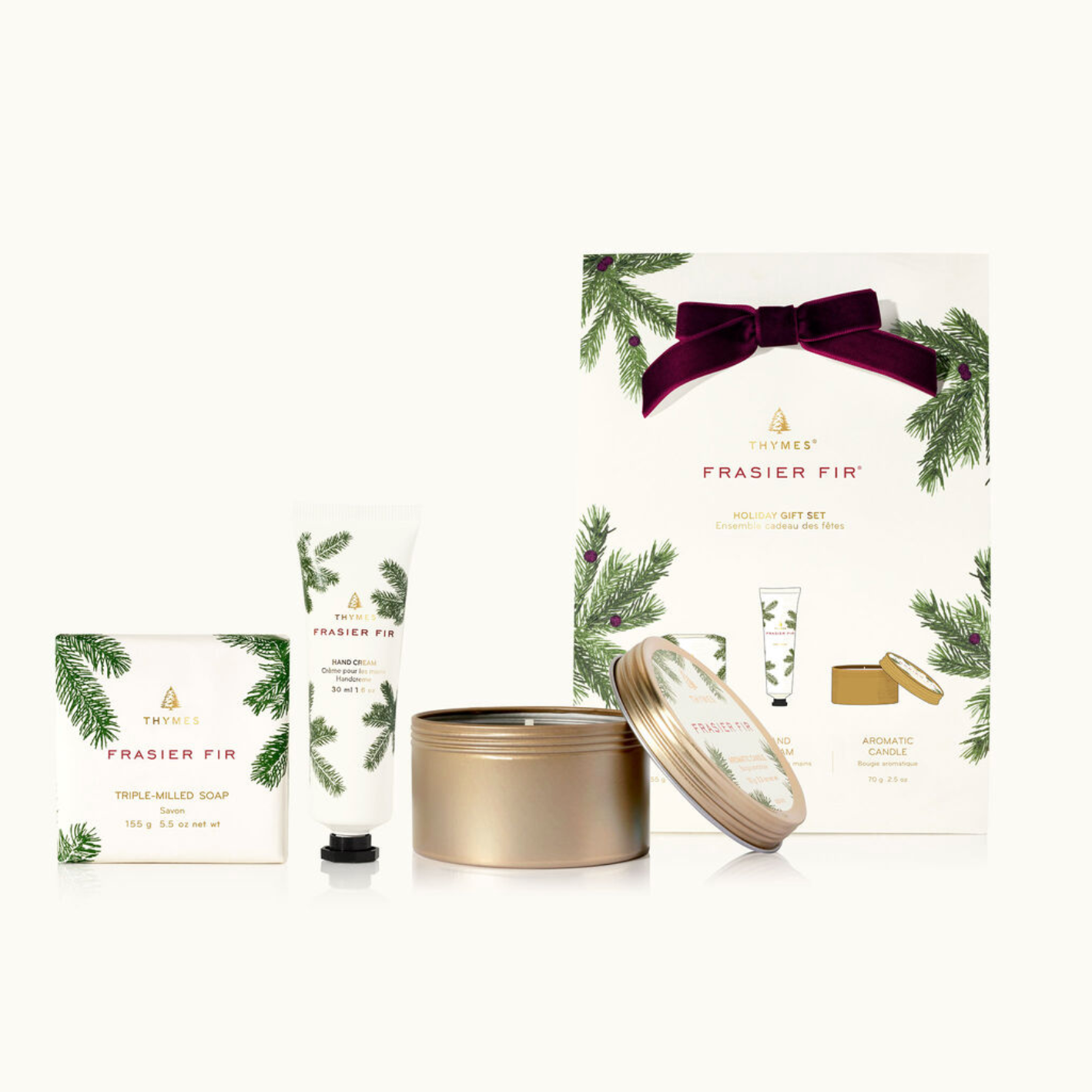 A Thymes Holiday Gift Set which includes a bar soap, petite hand cream, and a travel tin, all in Frasier Fir fragrance. The packaging is primarily white and green with a gold bow on top.