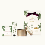 A Thymes Holiday Gift Set which includes a bar soap, petite hand cream, and a travel tin, all in Frasier Fir fragrance. The packaging is primarily white and green with a gold bow on top.