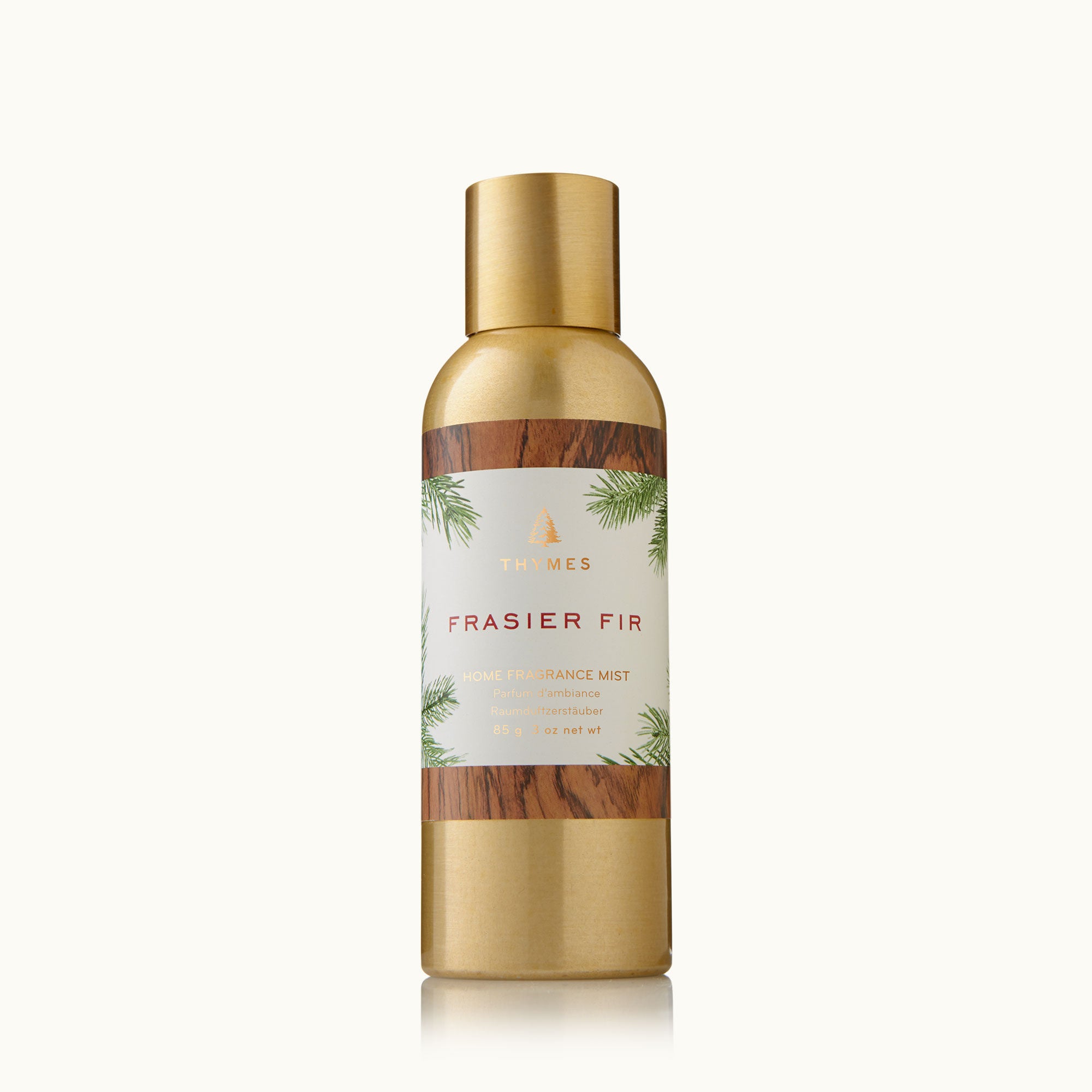 A bottle of Thymes Frasier Fir Home Fragrance Mist with a gold cap and label featuring green pine needles. Available at Be Charmed