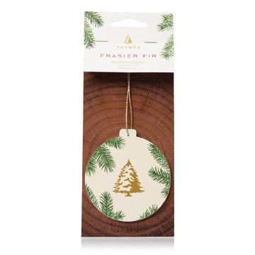 A round Thymes Frasier Fir sachet with a Christmas tree and pine needles design, packaged in a card with the brand name visible. Available at Be Charmed