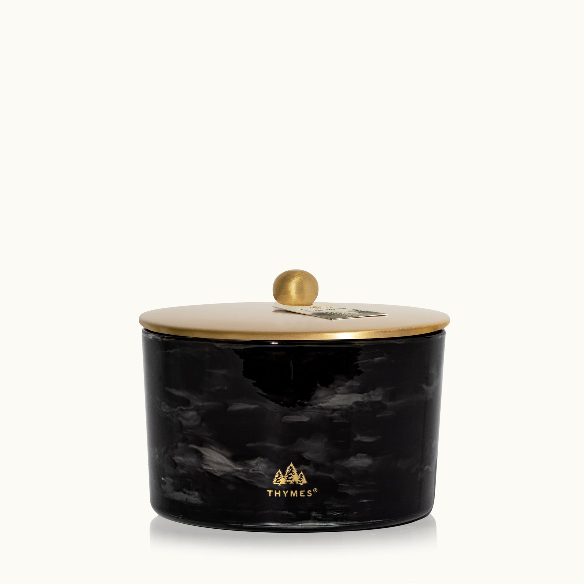 Black marbled candle jar with gold lid on a white background, featuring the Thymes logo. Available at Be Charmed.  