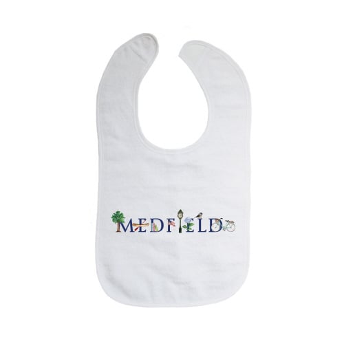 A white cotton bib with velcro closure, featuring the text 'MEDFIELD' and some decorative elements in blue and green. Available at Be Charmed