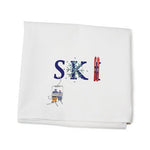 A white cotton kitchen towel with 'SKI' printed in blue, accompanied by a small graphic of skiis. Available at Be Charmed