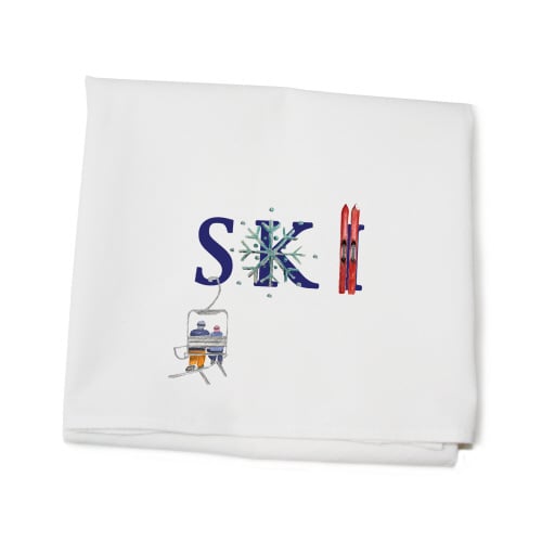 A white cotton kitchen towel with 'SKI' printed in blue, accompanied by a small graphic of skiis. Available at Be Charmed