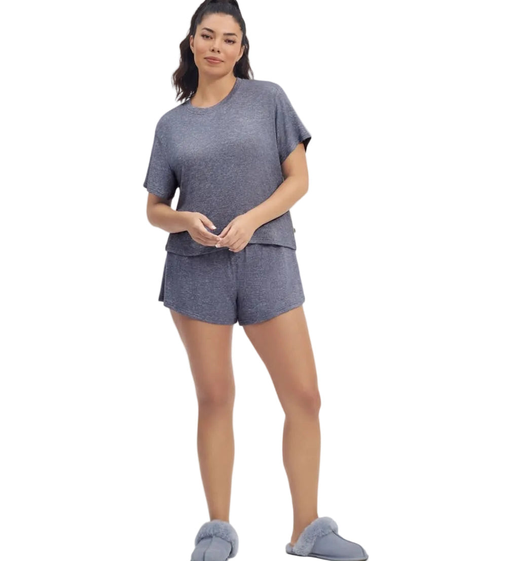 A woman standing and wearing a navy heather gray UGG Aniyah sleepwear set, consisting of a boxy fit tee and matching sleep shorts with a ruffle waistband. Available at Be Charmed