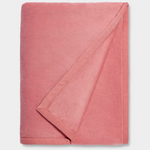 A pink UGG Duffield II throw blanket with a subtle leather-like finish on the edges, folded loosely. Available at Be Charmed