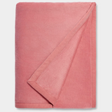 A pink UGG Duffield II throw blanket with a subtle leather-like finish on the edges, folded loosely. Available at Be Charmed