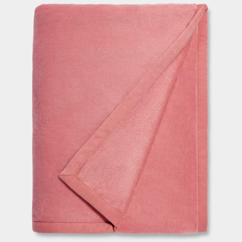 A pink UGG Duffield II throw blanket with a subtle leather-like finish on the edges, folded loosely. Available at Be Charmed