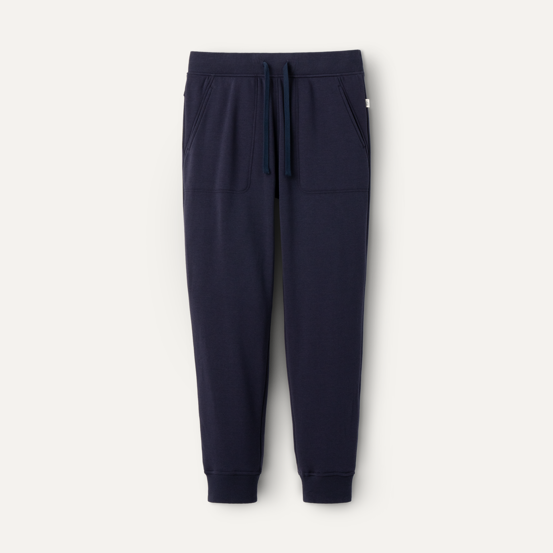 A pair of navy blue UGG men's jogger pants with a drawstring waist and a brand tag on the lower left side. Available at Be Charmed