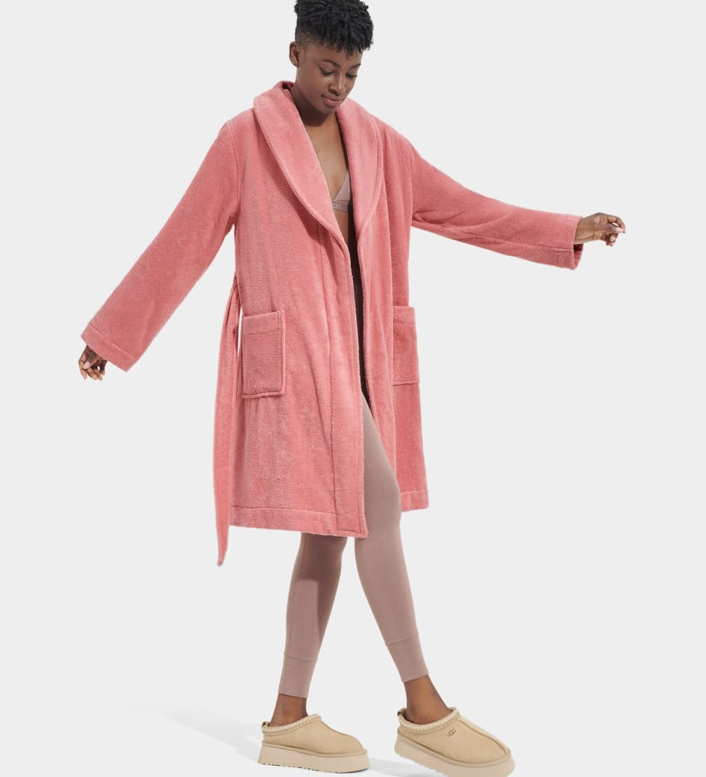 A model wearing a pink UGG Lenore Terry Robe with traditional patch pockets and an embroidered UGG heritage logo. Available at Be Charmed