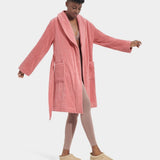 A model wearing a pink UGG Lenore Terry Robe with traditional patch pockets and an embroidered UGG heritage logo. Available at Be Charmed