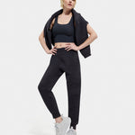 A female model standing, posing, and turning to face the camera. She is wearing a black UGG Ink Sofiana Mixed Jogger with an elastic waistband, and white sneakers. Available at Be Charmed