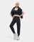 A female model standing, posing, and turning to face the camera. She is wearing a black UGG Ink Sofiana Mixed Jogger with an elastic waistband, and white sneakers. Available at Be Charmed