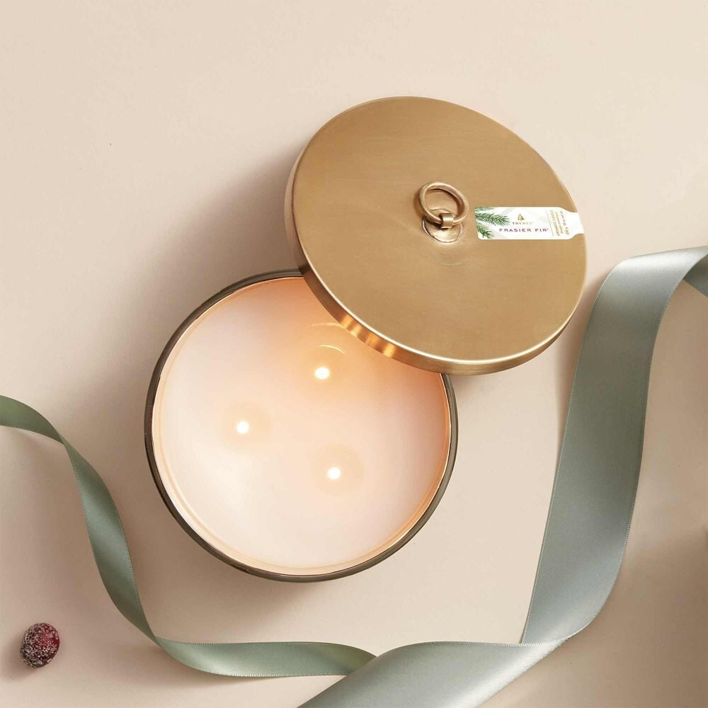 View of lit Thymes Frasier Fir Frosted Plaid 3-Wick Candle with festive holiday scent – Available at Be Charmed