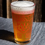Pint glass of pale ale with decorative text on a wooden surface. Available at Be Charmed