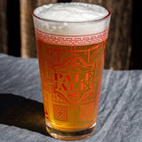 Pint glass of pale ale with decorative text on a wooden surface. Available at Be Charmed