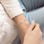 Close-up of a hand wearing a silver bracelet with heart designs. Available at Be Charmed