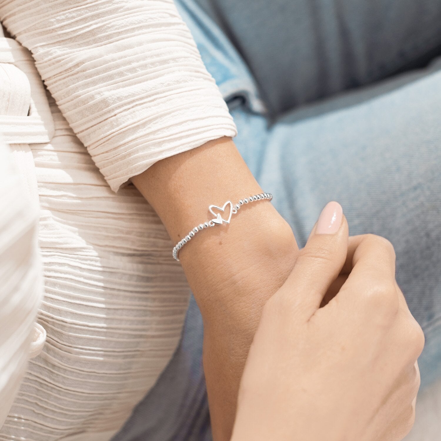 Close-up of a hand wearing a silver bracelet with heart designs. Available at Be Charmed