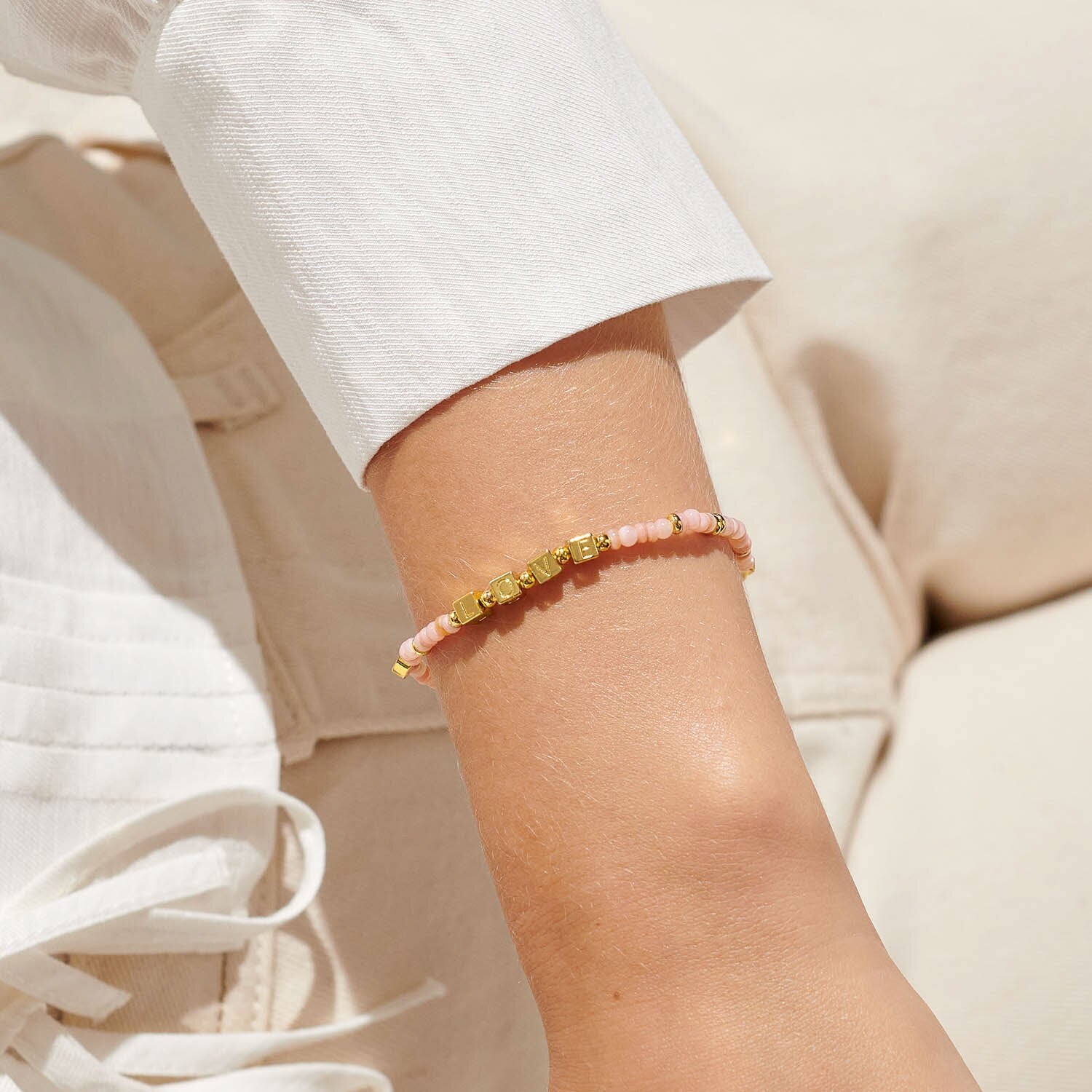 Close-up of a wrist wearing a pink beaded bracelet with gold accents on a neutral background. Available at Be Charmed
