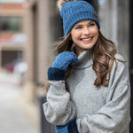 Woman wearing A pair of blue cozy cable knit mittens with a plush lining and cuff. Available at Be Charmed