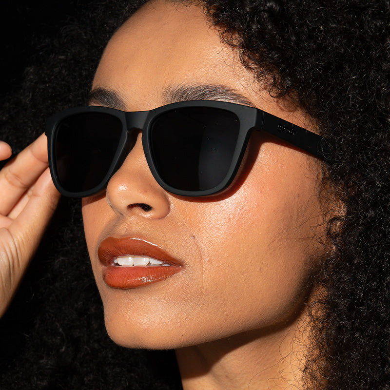 A person wearing black Goodr square-framed sunglasses. Avaiable at Be Charmed