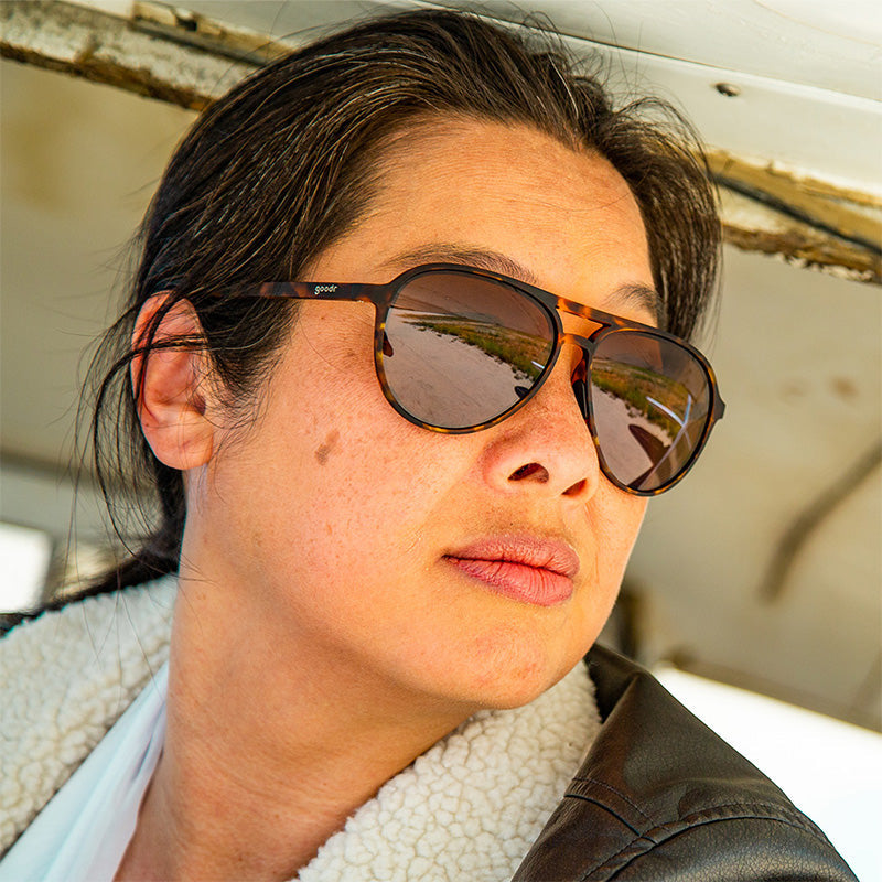 Woman wearing 

Goodr aviator-style sunglasses named "Amelia Earhart Ghosted Me" with polarized lenses and matte black frames—fashion meets function at Be Charmed.