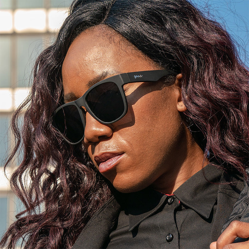 Woman wearing Goodr Hooked On Onyx sunglasses featuring matte black frames, polarized lenses, and a no-slip, no-bounce design—performance meets style at Be Charmed.
