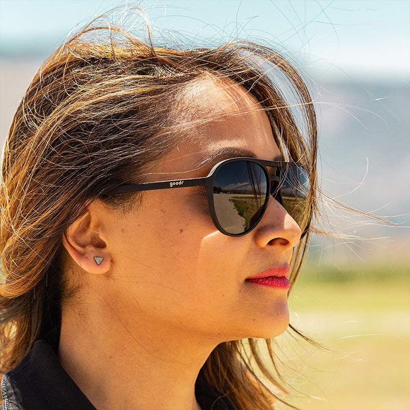 Woman wearing Operation Blackout Goodr sunglasses with all-black polarized lenses and matte black no-slip frames—sleek performance shades; available at Be Charmed