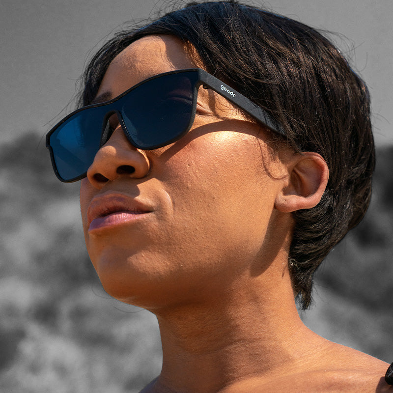 Woman wearing Goodr The Future is Void Sunglasses with sleek matte black frames and polarized lenses, offering futuristic style and athletic comfort, available at Be Charmed