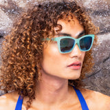 Woman wearing Goodr Will Brake For Mermaids Sunglasses with ttranslucent teal frames and reflective tealpolarized lenses, combining playful ocean vibes and performance fit, available at Be Charmed