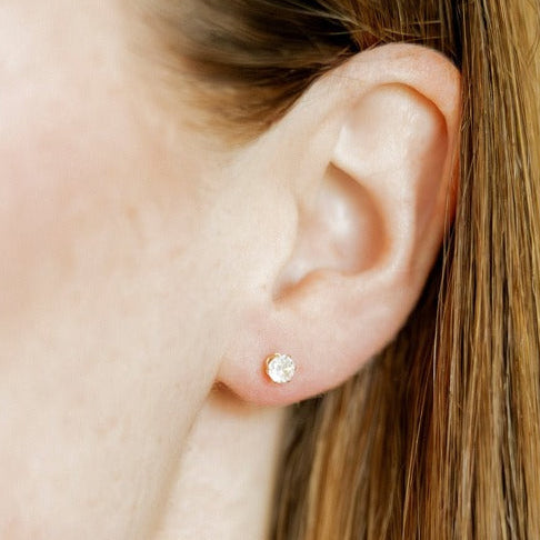 Close-up of an ear wearing a diamond stud earring on a white background. Available at Be Charmed