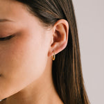 Woman wearing Lover's Tempo Evie 15mm gold hoop earrings with sleek finish, available at Be Charmed.