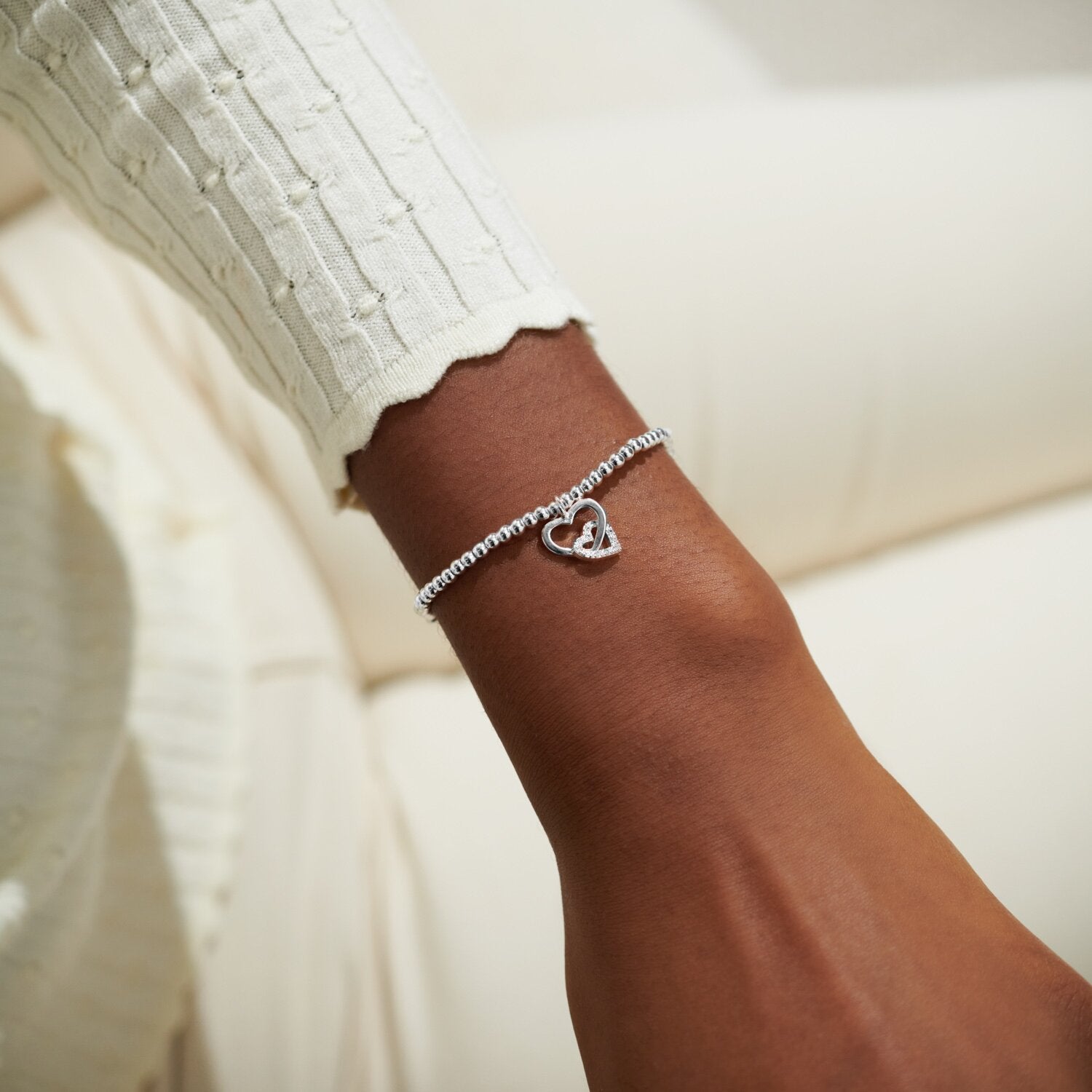 Silver heart bracelet on a wrist with a blurred background. Available at Be Charmed