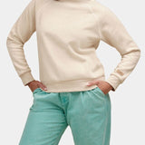 Person wearing a beige sweater and teal pants on a white background. Available at Be Charmed