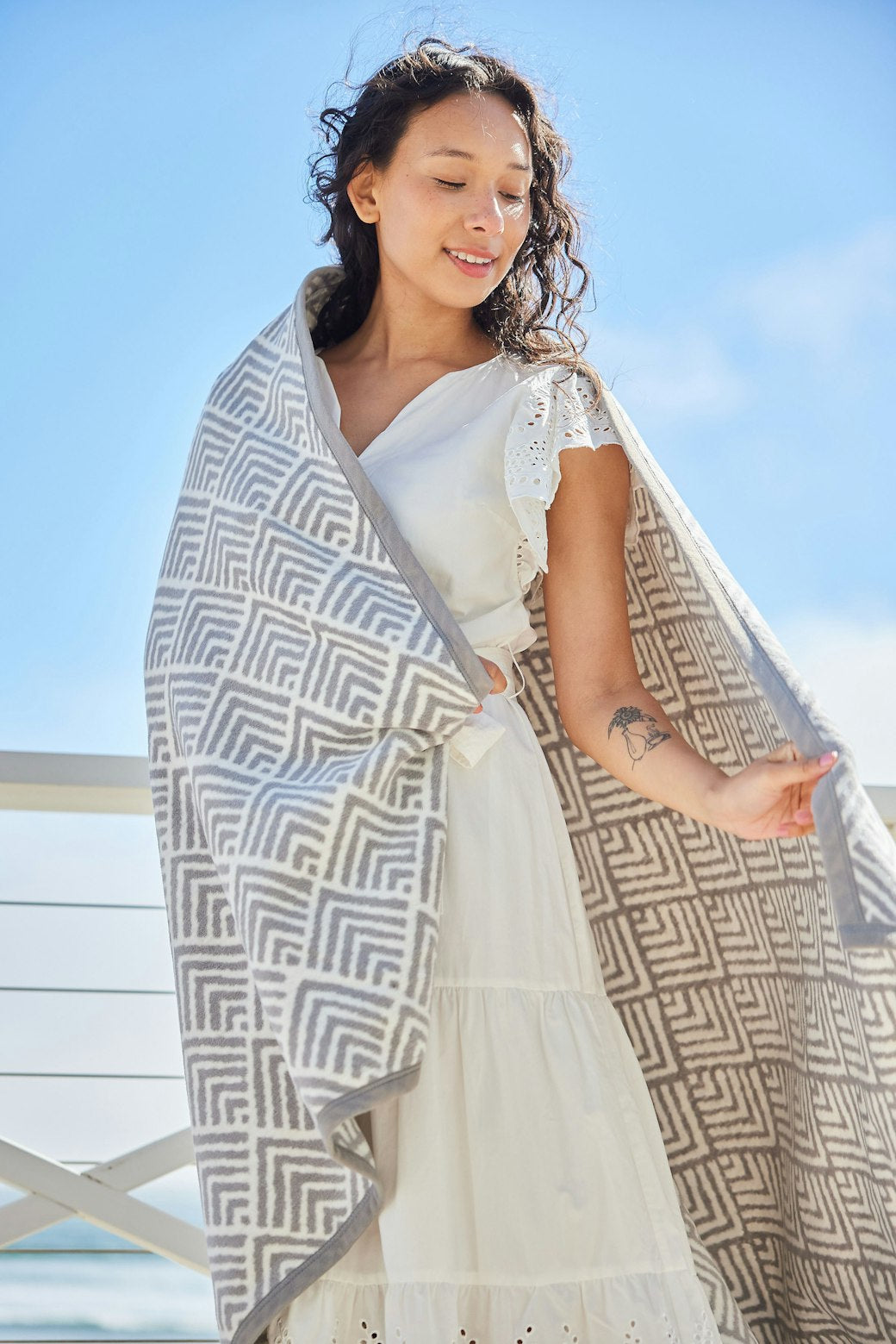 Woman wrapped in Oyster Cove Grey ChappyWrap Blanket featuring a classic diamond weave pattern, made from a cotton-blend fabric for exceptional softness and durability—ideal for cozy nights or elegant home décor. Available at Be Charmed.