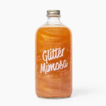 Bottle of 'Wood Stove Kitchen's Glitter Mimosa' on a white background. Available at Be Charmed