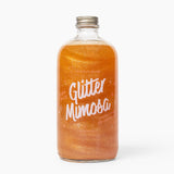 Bottle of 'Wood Stove Kitchen's Glitter Mimosa' on a white background. Available at Be Charmed