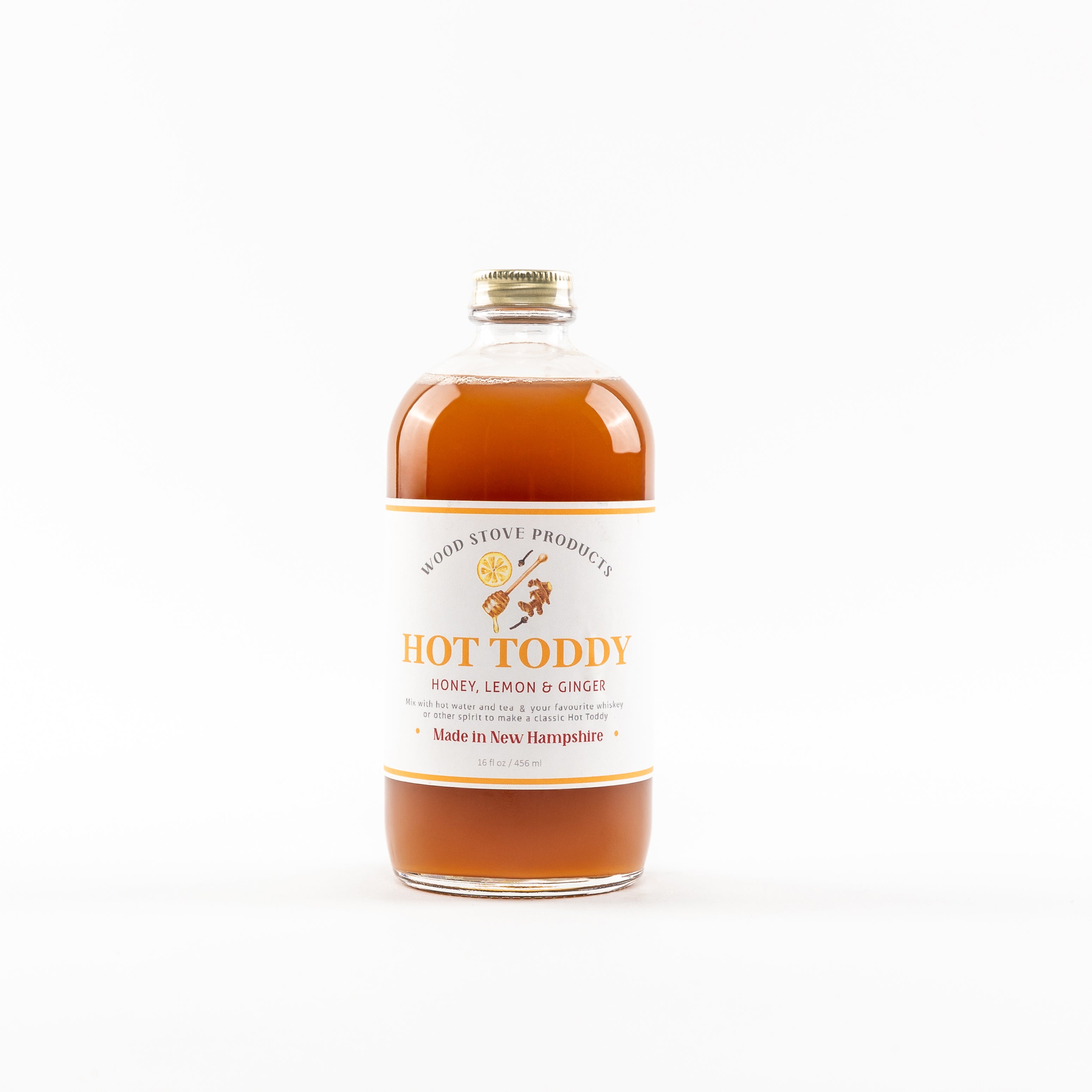 A bottle of Hot Toddy Mix by Wood Stove Kitchen, featuring lemon & ginger, with a label that includes the product name and a graphic of a toddy. Available of Be Charmed