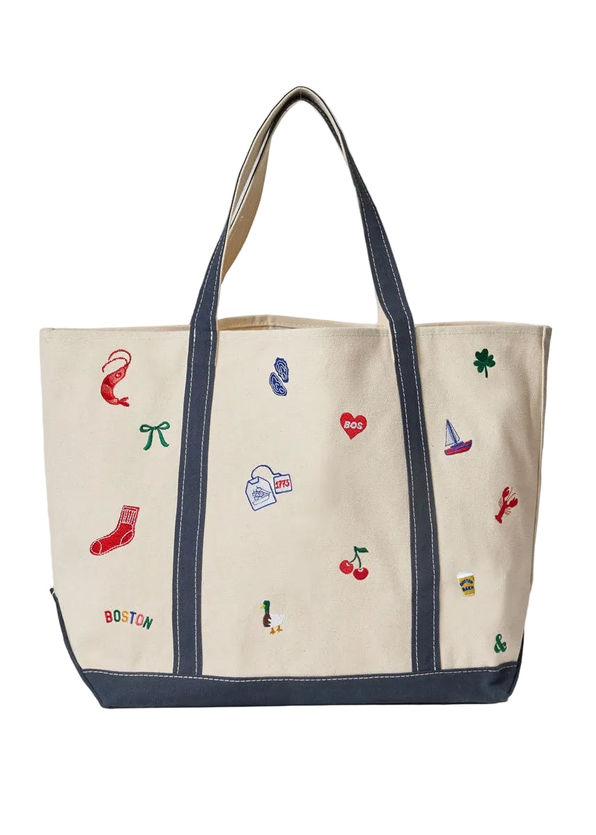 An Alice & Wonder canvas tote bag with dark navy blue trim, handles, and bottom panel, decorated with colorful embroidered motifs including a red sock, cherries, a clover, and a small sailboat. The word 'BOSTON' is embroidered in multicolor letters near the bottom left. Available at Be Charmed