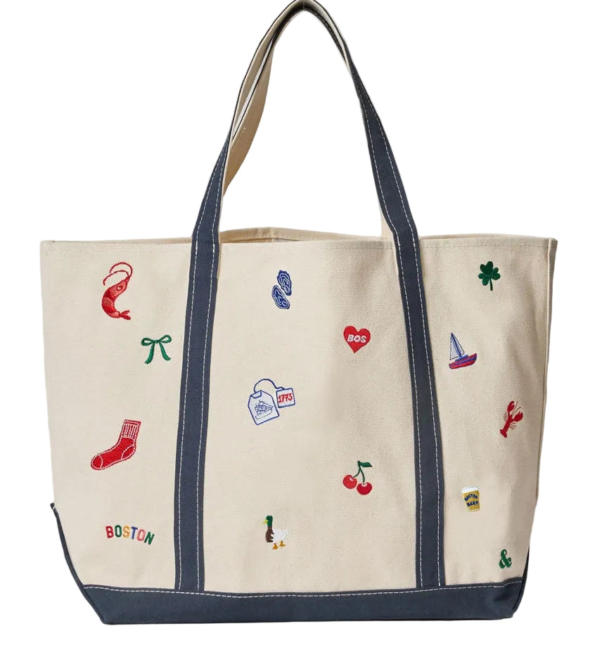 An Alice & Wonder canvas tote bag with dark navy blue trim, handles, and bottom panel, decorated with colorful embroidered motifs including a red sock, cherries, a clover, and a small sailboat. The word 'BOSTON' is embroidered in multicolor letters near the bottom left. Available at Be Charmed