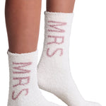 White fuzzy socks with pink Mrs text worn by a person on a light gray background. Mrs Wedding fuzzy socks. Available at Be Charmed. 