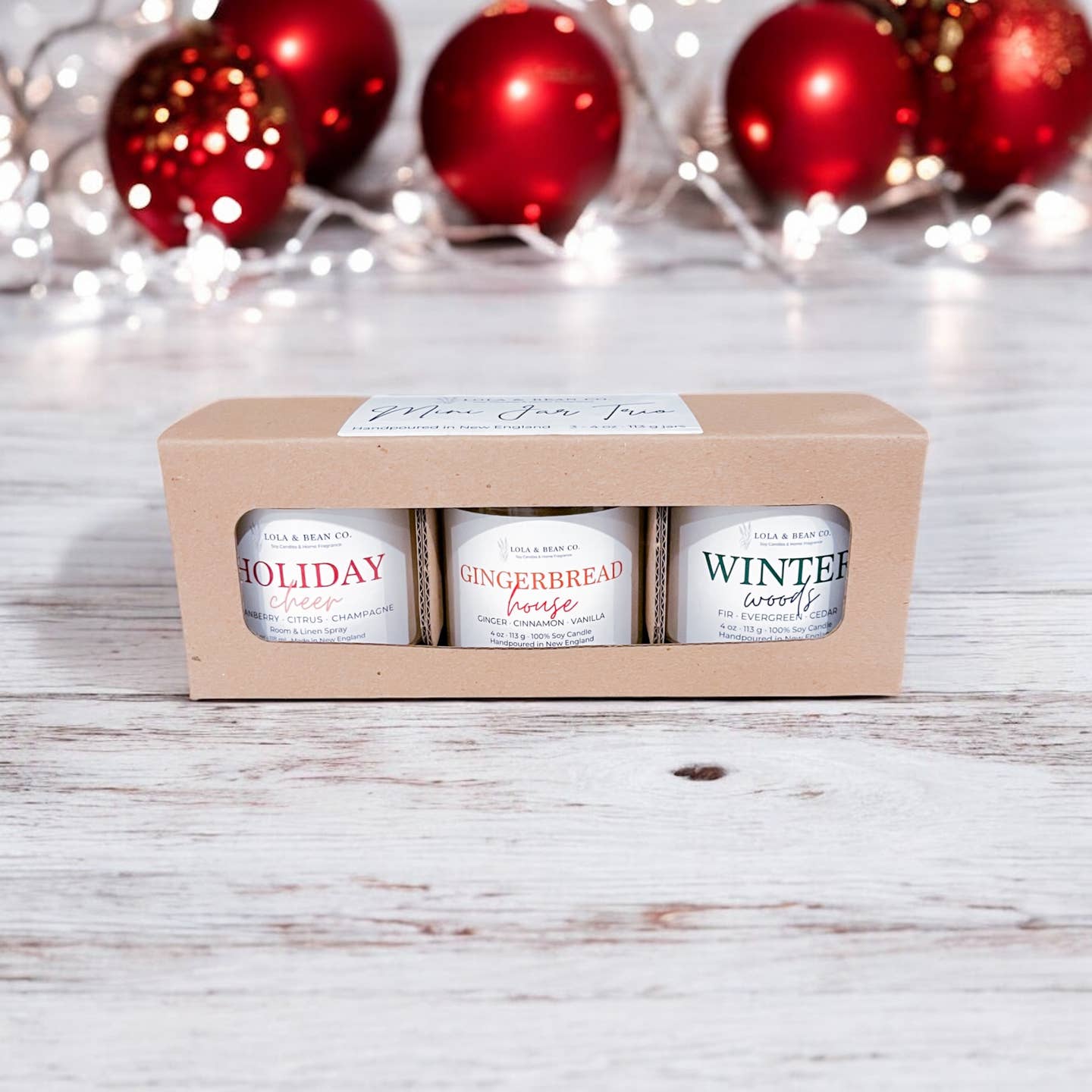  Lola & Bean boxed mini candle trio with Holiday Cheer, Gingerbread House, and Winter Woods, with red ornaments behind it. Available at Be Charmed.